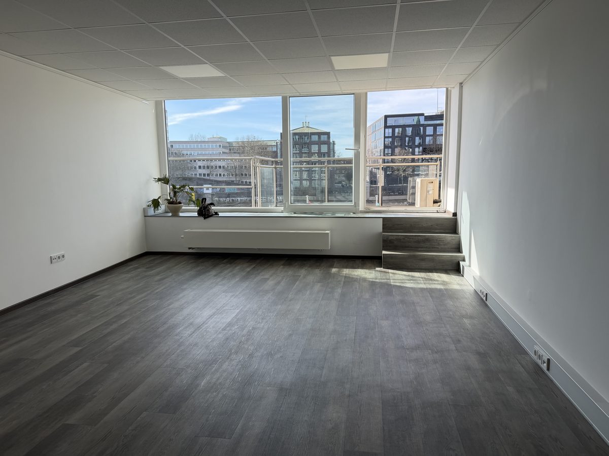 Leerstehende Bürofläche am Fensterband mit Rasterdecke, dunklem Vinylboden und Bestandspodest